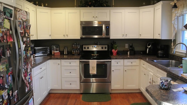 kitchen with white cabinets, stainless steel appliances, a sink, and wood finished floors