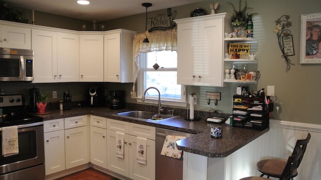 kitchen featuring decorative light fixtures, dark countertops, appliances with stainless steel finishes, white cabinets, and a sink