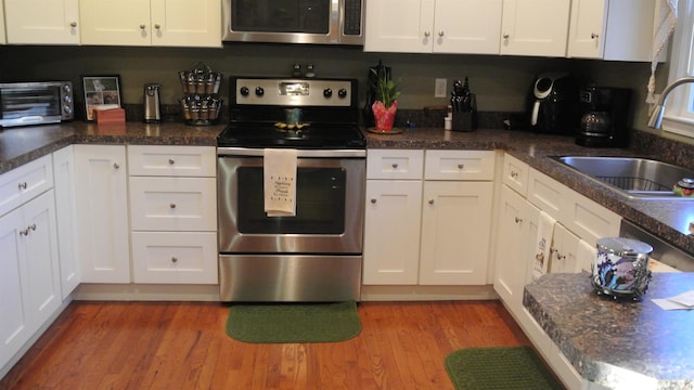 kitchen with a toaster, stainless steel appliances, a sink, white cabinets, and light wood-style floors