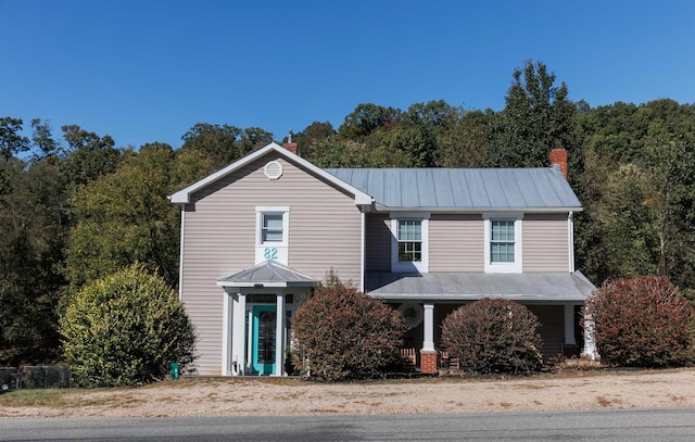 traditional-style house featuring a chimney, metal roof, and a standing seam roof
