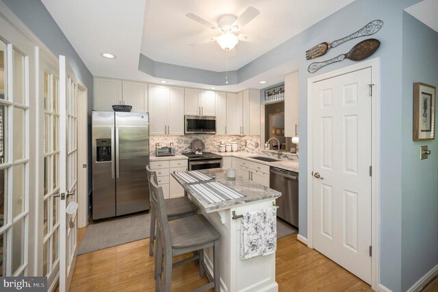 9404 Dalmahoy Ln, Fredericksburg, VA 22408 - kitchen with appliances with stainless steel finishes, a sink, light wood-style floors, tasteful backsplash, and a kitchen island