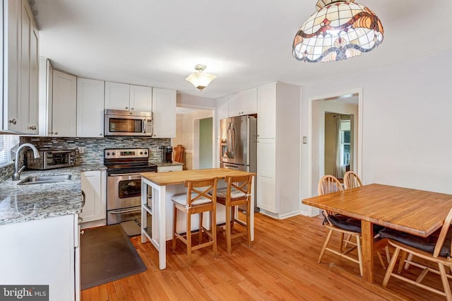  - kitchen featuring appliances with stainless steel finishes, light wood-type flooring, backsplash, white cabinets, and light stone countertops