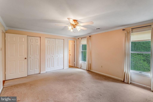  - unfurnished bedroom with multiple closets, ornamental molding, carpet, and a ceiling fan