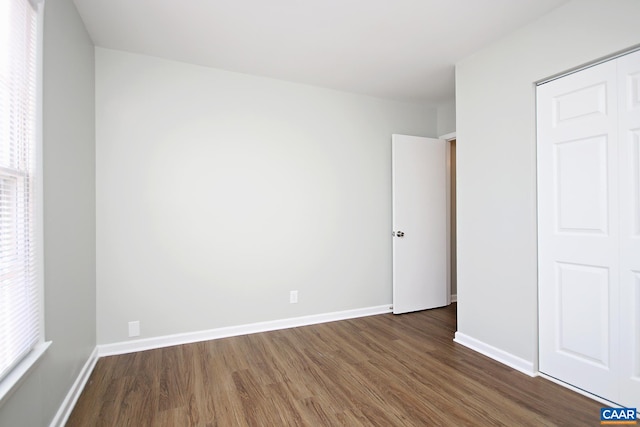 unfurnished bedroom featuring dark wood-style flooring, baseboards, a closet, and multiple windows