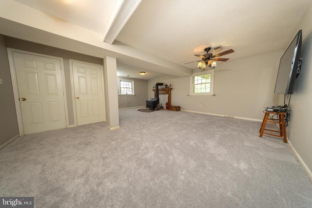  - unfurnished living room featuring a wood stove, ceiling fan, carpet floors, and beam ceiling