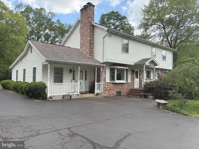  - view of front of house with a chimney, covered porch, brick siding, and asphalt driveway