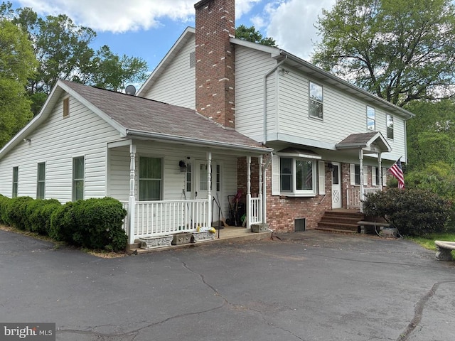  - view of front facade featuring a porch, a chimney, and brick siding