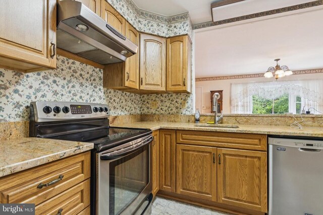  - kitchen with appliances with stainless steel finishes, under cabinet range hood, wallpapered walls, and brown cabinetry