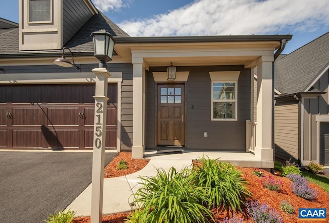 entrance to property with a porch, driveway, a garage, and roof with shingles