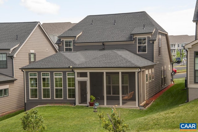rear view of house with a shingled roof, a sunroom, and a lawn
