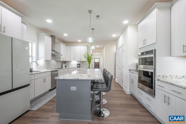 kitchen with appliances with stainless steel finishes, a sink, wall chimney range hood, a center island, and a breakfast bar