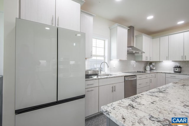 kitchen featuring freestanding refrigerator, wall chimney exhaust hood, a sink, backsplash, and stainless steel dishwasher