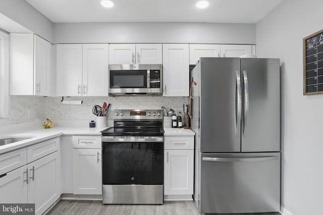 kitchen featuring stainless steel appliances, white cabinets, light countertops, light wood finished floors, and backsplash