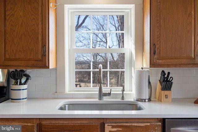  - kitchen featuring a sink, brown cabinets, dishwasher, and backsplash