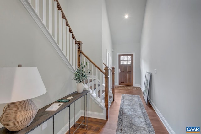 entryway featuring baseboards, stairs, a high ceiling, and wood finished floors