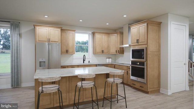 kitchen featuring light brown cabinets, a center island, stainless steel appliances, wall chimney exhaust hood, and a sink