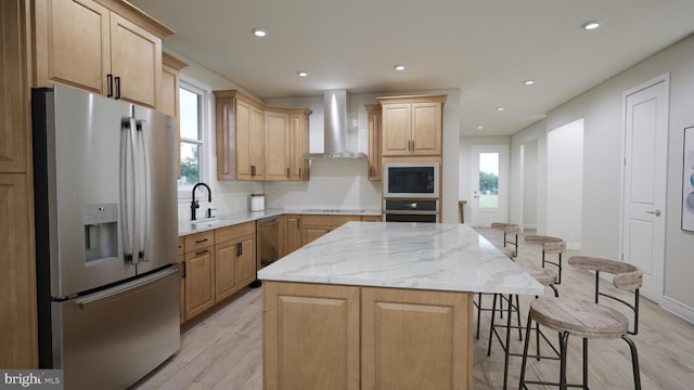 kitchen with a kitchen island, a breakfast bar, a sink, appliances with stainless steel finishes, and wall chimney range hood