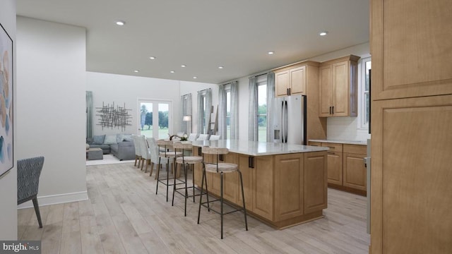 kitchen featuring light wood-style flooring, stainless steel fridge, a breakfast bar area, and light countertops