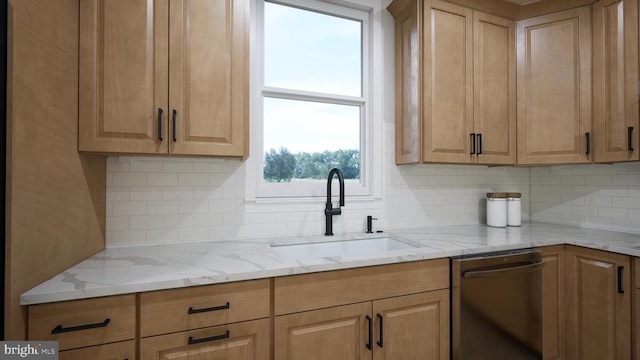 kitchen featuring light stone counters, light brown cabinetry, a sink, stainless steel dishwasher, and backsplash