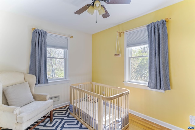 bedroom with wood finished floors, a ceiling fan, baseboards, and a crib