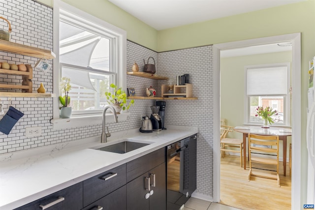 kitchen with a sink, open shelves, black dishwasher, backsplash, and light stone counters