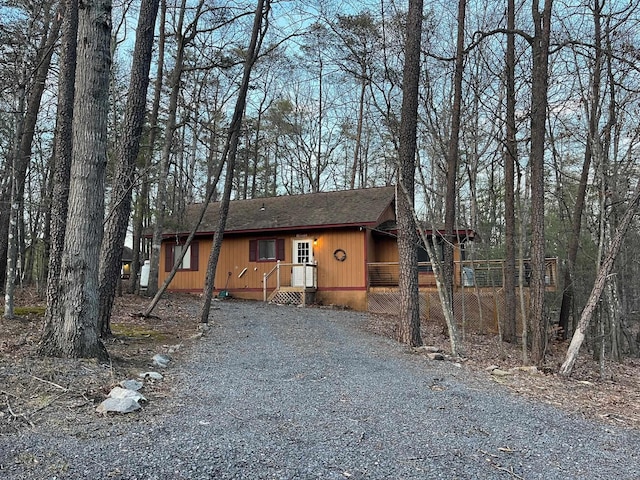 rustic home featuring roof with shingles and gravel driveway