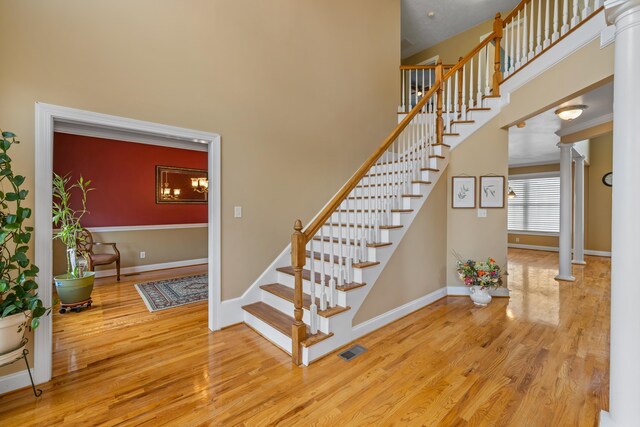 stairway with wood finished floors, a high ceiling, baseboards, decorative columns, and a chandelier