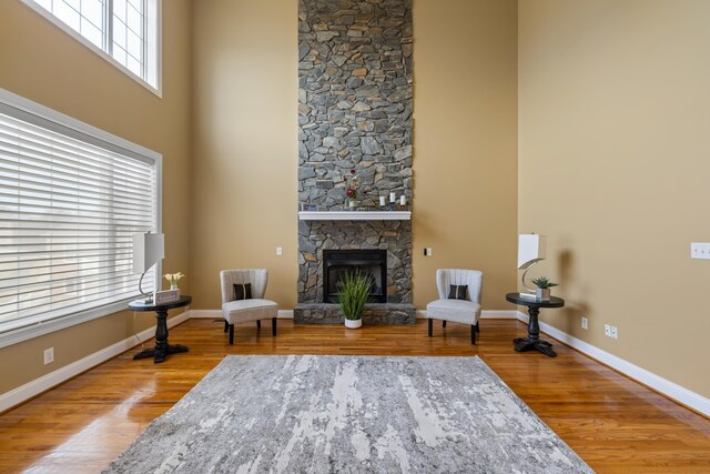 sitting room with baseboards, wood finished floors, a towering ceiling, and a stone fireplace