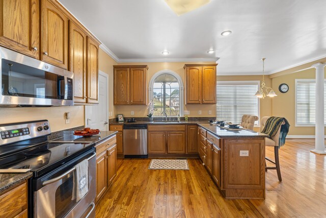 kitchen with a sink, brown cabinetry, wood finished floors, a breakfast bar, and appliances with stainless steel finishes