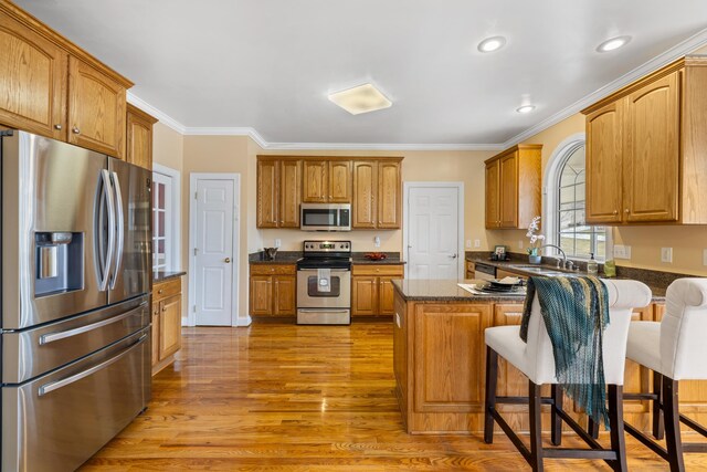 kitchen featuring a breakfast bar area, a peninsula, crown molding, light wood-style floors, and appliances with stainless steel finishes