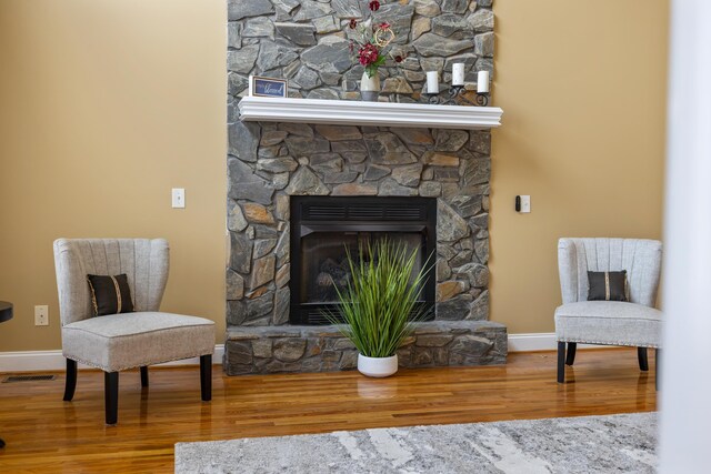 living area featuring wood finished floors, visible vents, baseboards, and a stone fireplace