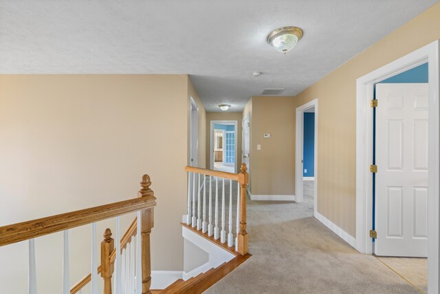 corridor featuring light colored carpet, baseboards, an upstairs landing, and visible vents
