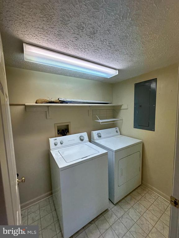 clothes washing area featuring electric panel, washing machine and dryer, a textured ceiling, and baseboards