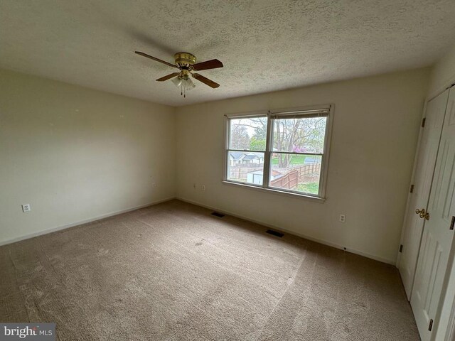 empty room with a ceiling fan, carpet floors, a textured ceiling, and baseboards