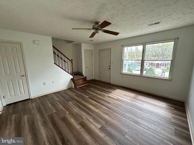 unfurnished living room with stairway, wood finished floors, a ceiling fan, baseboards, and a textured ceiling