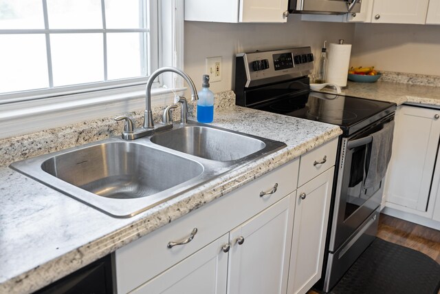 kitchen featuring stainless steel range with electric stovetop, a sink, and white cabinetry