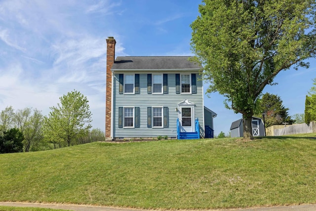 colonial home with a chimney, a storage unit, an outdoor structure, and entry steps