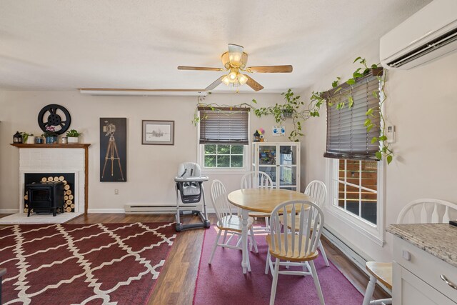 dining space with a wall mounted AC, a baseboard radiator, wood finished floors, ceiling fan, and a wood stove