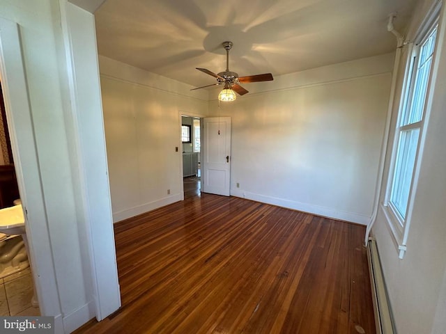 empty room with a baseboard heating unit, dark wood finished floors, baseboards, and a ceiling fan