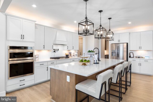 10103 N Streamview Ct, Fredericksburg, VA 22408 - kitchen featuring stainless steel appliances, a chandelier, premium range hood, light wood-style flooring, and a kitchen island with sink
