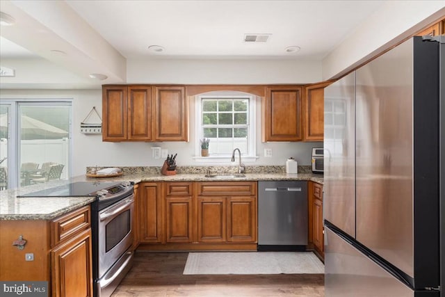  - kitchen with appliances with stainless steel finishes, brown cabinetry, a peninsula, and light stone countertops