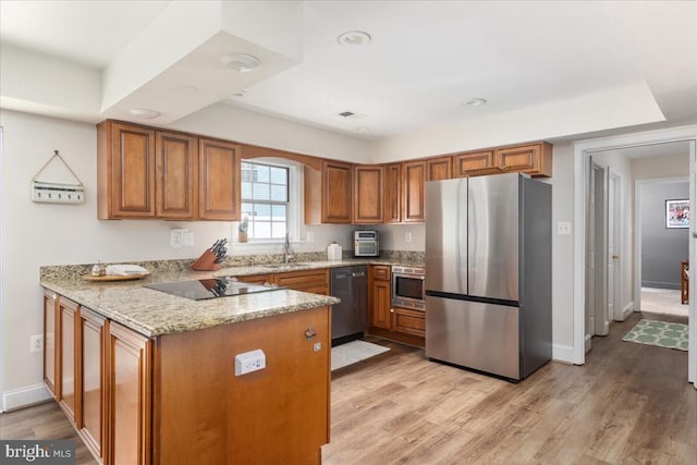  - kitchen featuring stainless steel appliances, brown cabinets, a peninsula, light stone counters, and light wood-type flooring