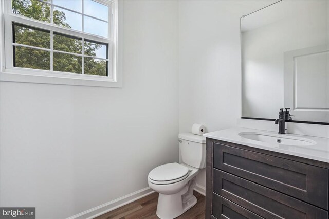  - half bathroom featuring wood finished floors, toilet, baseboards, and vanity