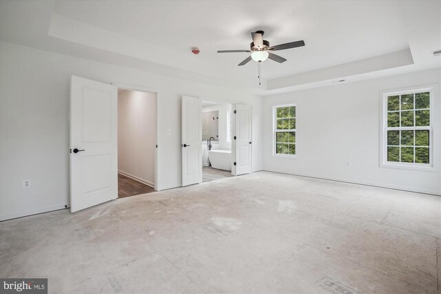  - unfurnished bedroom with a tray ceiling, ensuite bath, a ceiling fan, and baseboards