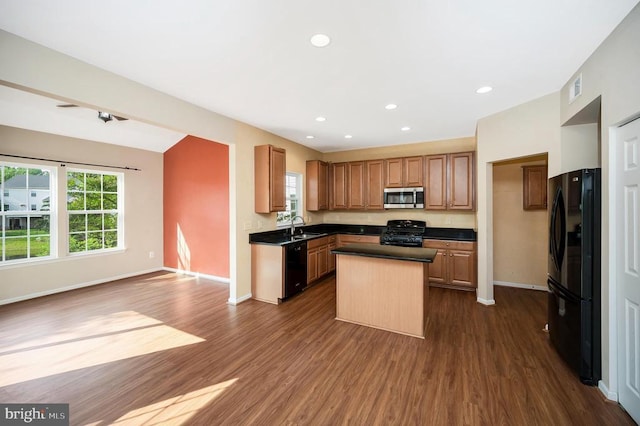  - kitchen featuring black appliances, dark countertops, a center island, dark wood finished floors, and healthy amount of natural light