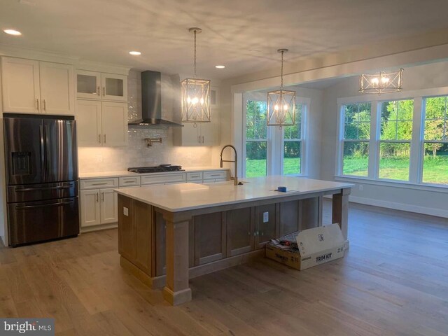 kitchen with black fridge with ice dispenser, wall chimney exhaust hood, a sink, light countertops, and healthy amount of natural light