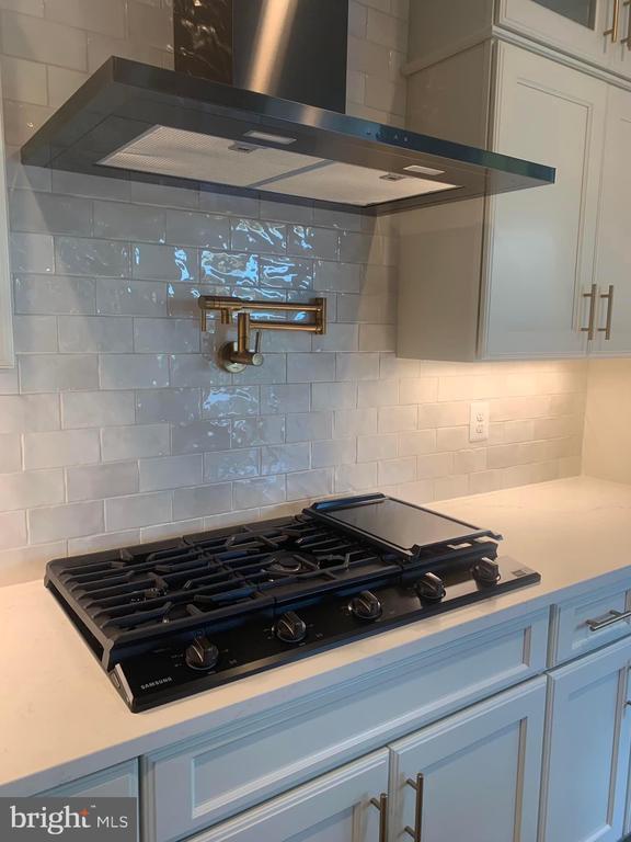 kitchen featuring wall chimney range hood, black gas cooktop, decorative backsplash, light countertops, and white cabinetry