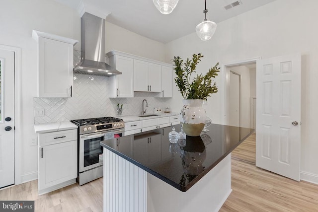 kitchen featuring stainless steel range with gas stovetop, a sink, wall chimney range hood, decorative backsplash, and white cabinets