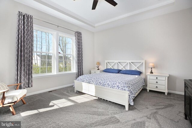 bedroom with dark colored carpet, a tray ceiling, crown molding, baseboards, and a ceiling fan
