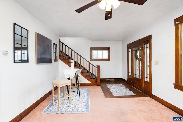 carpeted foyer entrance featuring baseboards, a ceiling fan, visible vents, and wood finished floors